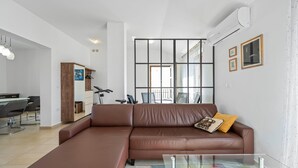 Un salon moderne avec un canapé en cuir marron, une table basse en verre et un coin repas comprenant une table et des chaises.