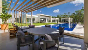 A modern outdoor patio with a pool, wooden pergola, and a view of a contemporary house.