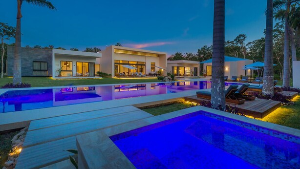 A modern house with a swimming pool, outdoor seating, and palm trees.