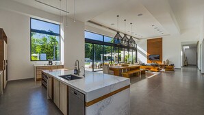 A modern kitchen with a large island, built-in appliances, and large windows offering a view of the outdoors.