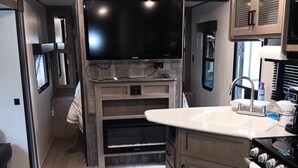 A compact RV kitchen with a large TV, built-in oven, and a sink. - Affordable stay 7 minutes to the beach 2021 32' RV (Navarre)
