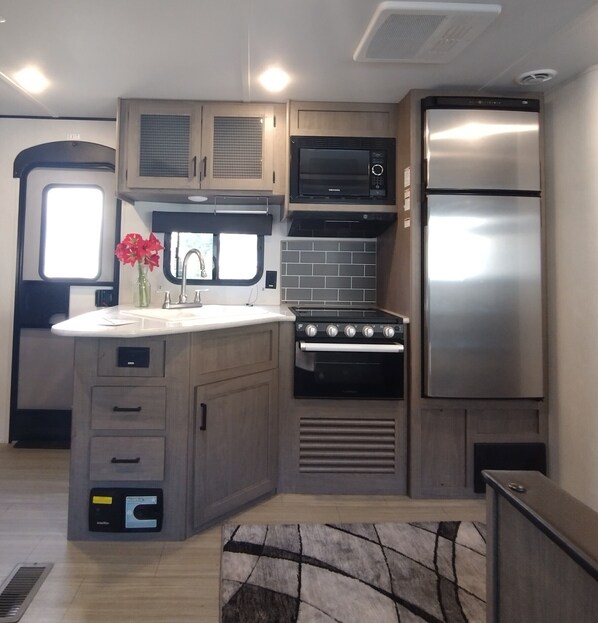 A compact kitchen with a built-in oven, microwave, and stainless steel refrigerator. - Affordable stay 7 minutes to the beach 2021 32' RV (Navarre)