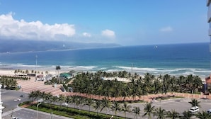 Vista costera con una carretera que lleva a una playa, palmeras y un faro distante.