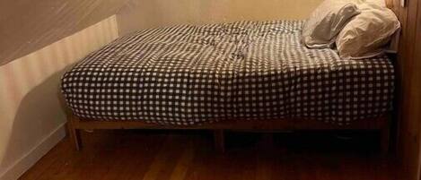A small, cozy room with a single bed, a window with checkered curtains, and a wooden floor.
