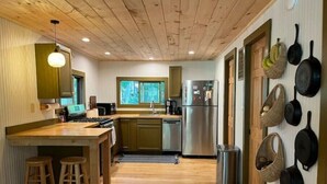 Une cuisine moderne avec un plancher en bois, un réfrigérateur en acier inoxydable et une fenêtre donnant sur un espace verdoyant.