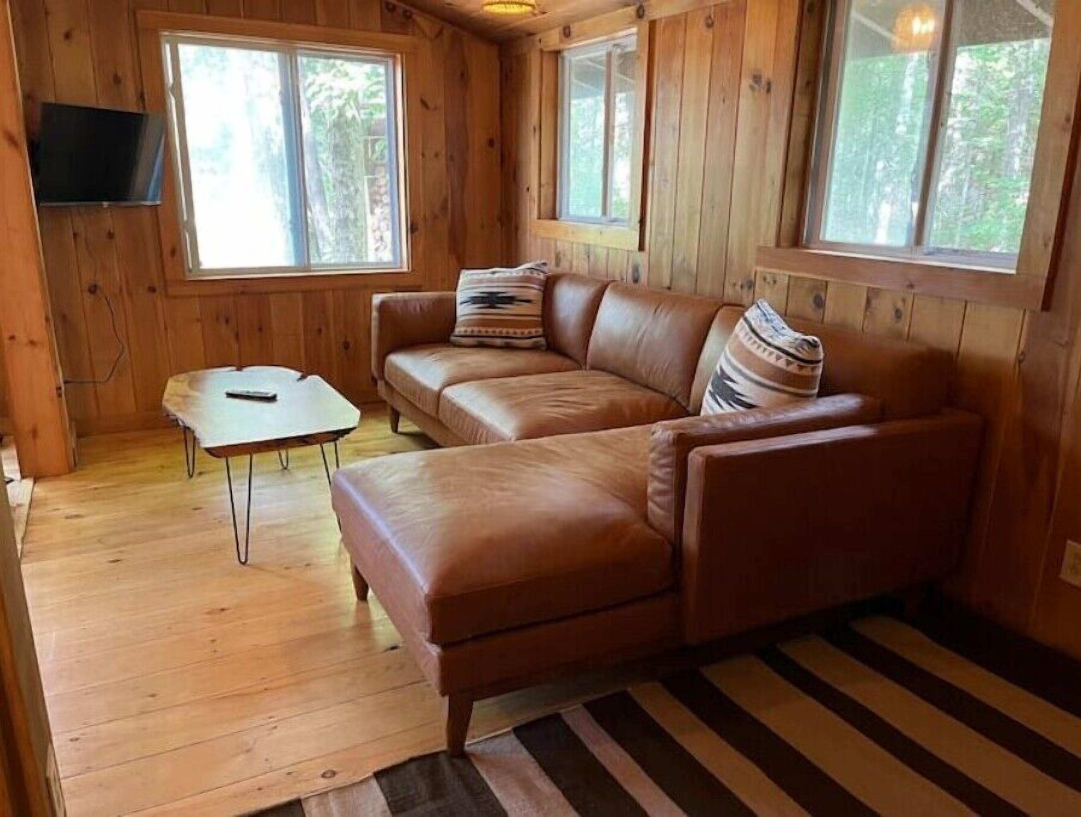 A wooden cabin interior with a brown leather couch, a small table, and a striped rug.