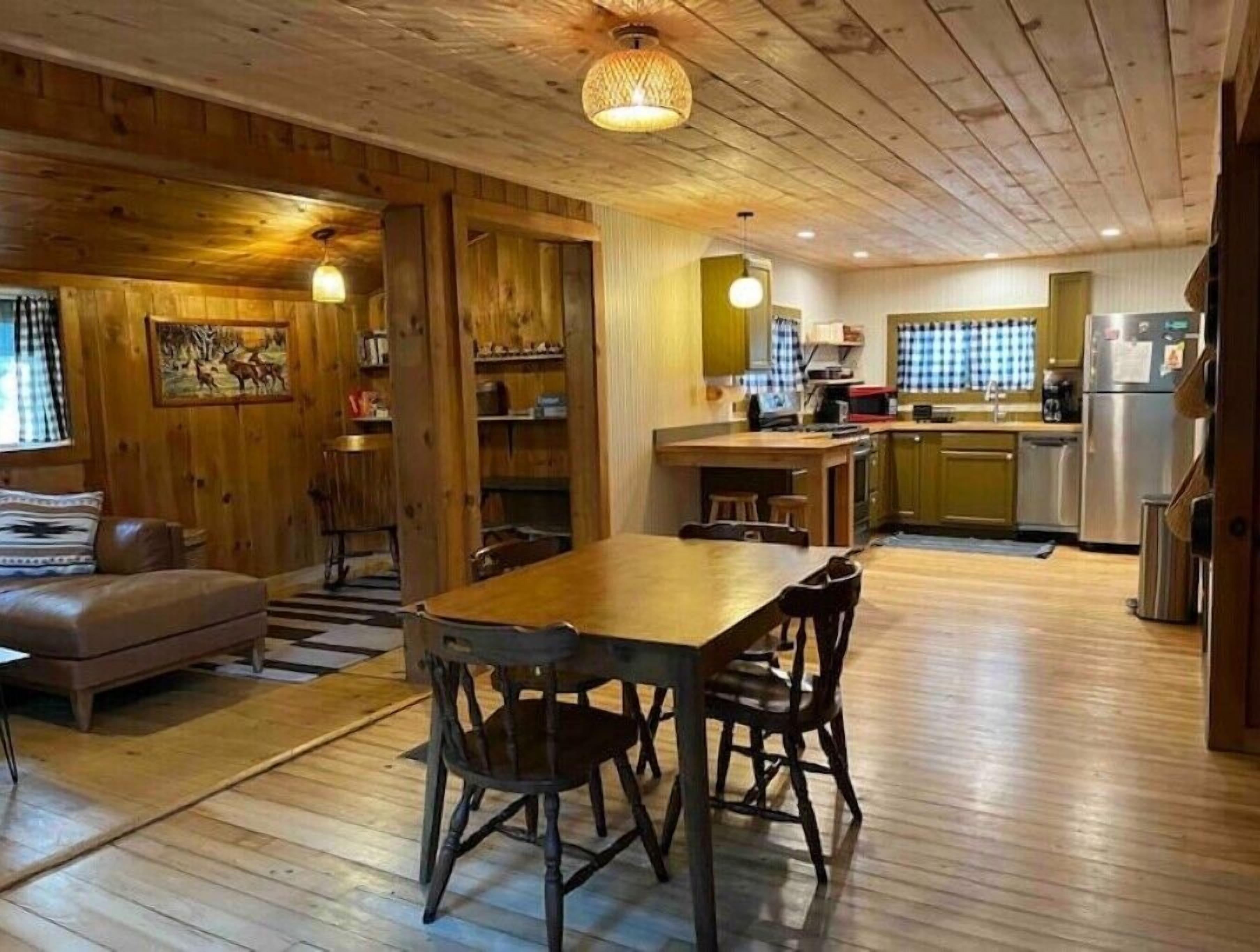 L’intérieur d’un chalet rustique comprend une table à manger en bois, des chaises, un canapé et un coin cuisine équipé d’un réfrigérateur et d’un four à micro-ondes.