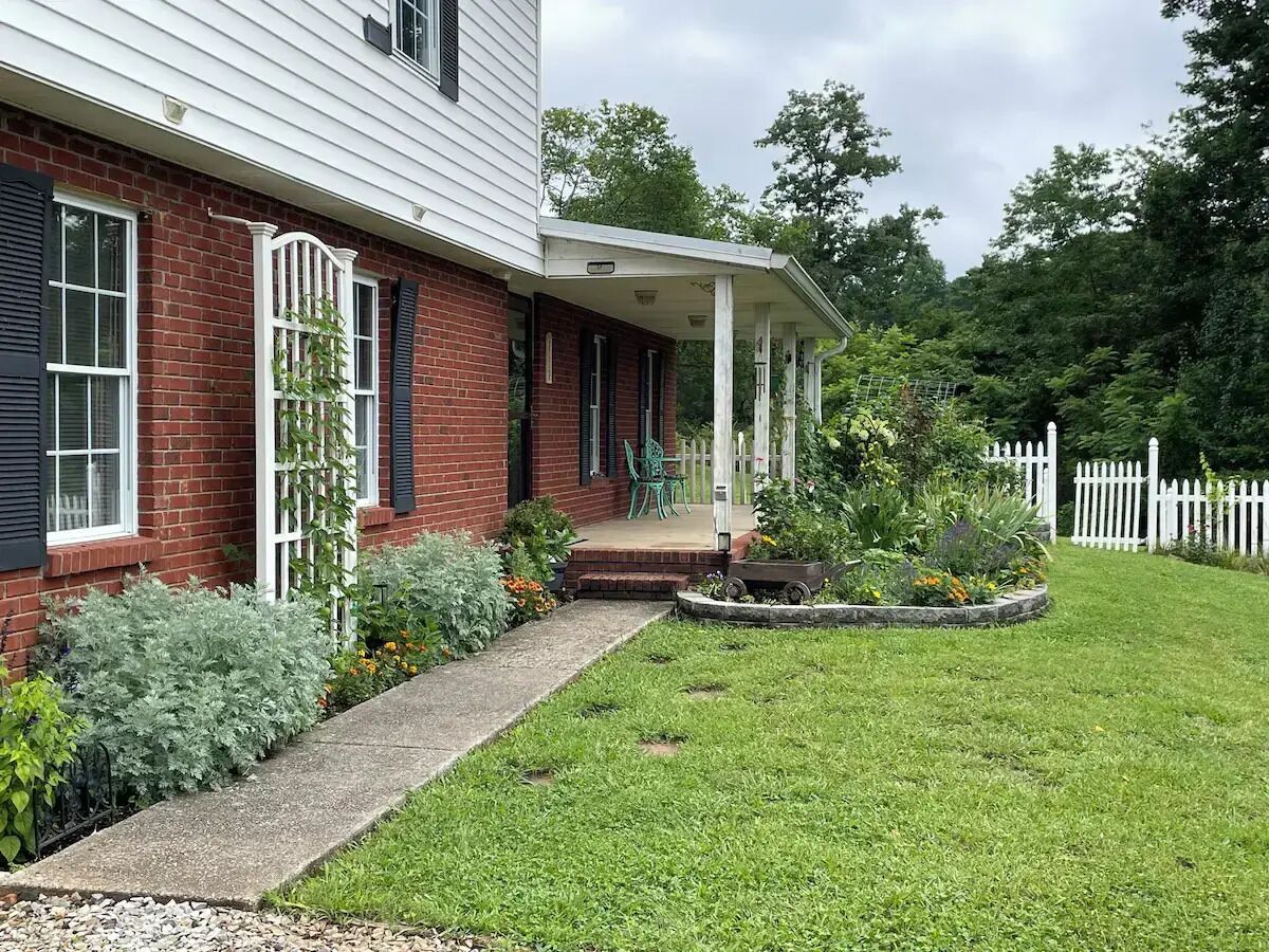 A two-story house with a brick facade, white siding, and a front porch with a white picket fence.