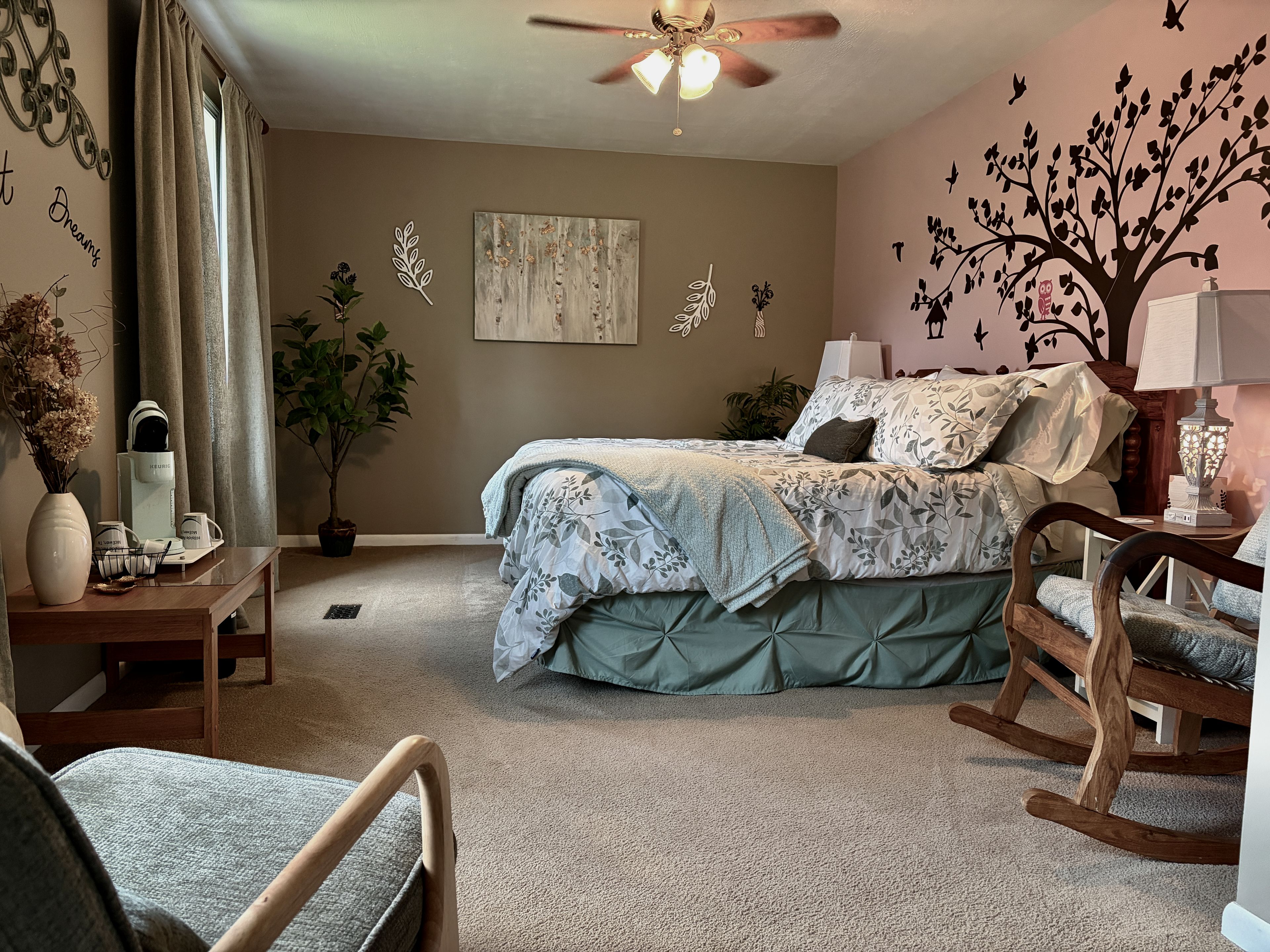 Ein Schlafzimmer mit Bett, Schaukelstuhl, Schreibtisch und Deckenventilator.