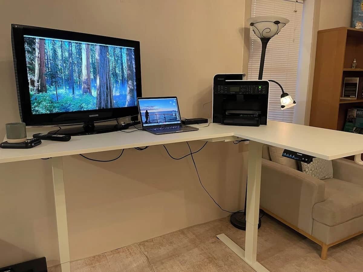 A desk with a computer monitor, laptop, and printer.