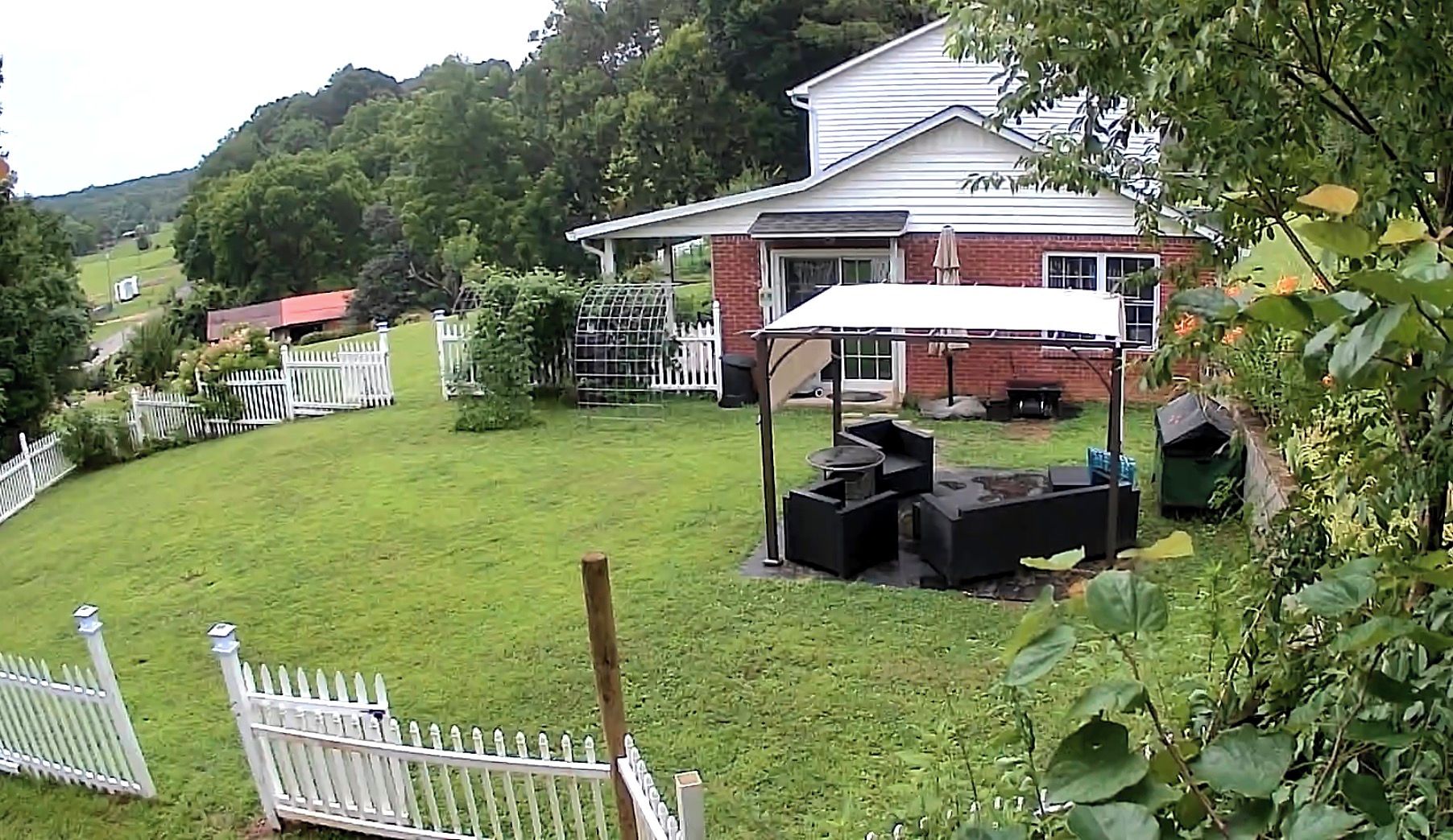 A residential property with a fenced backyard, a patio area with outdoor furniture, and a brick house.