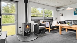 A cozy living room with a wood-burning stove, comfortable seating, and large windows offering a view of the outdoors. - Lovely home in Tarm with sauna (Tarm)