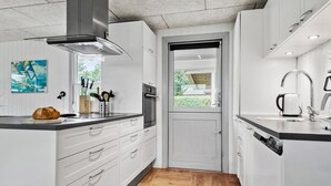 A modern kitchen with white cabinetry, a stainless steel range hood, a built-in oven, and a window with a view of greenery. - Lovely home in Tarm with sauna (Tarm)