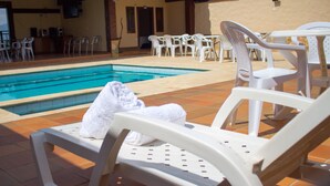 A poolside area with white plastic lounge chairs and a towel on one of them. - Hostal Hollywood Inn II (Rionegro)