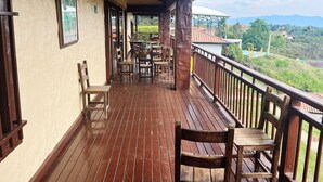 A wooden deck with tables and chairs, a railing, and a view of the landscape. - Hostal Hollywood Inn II (Rionegro)