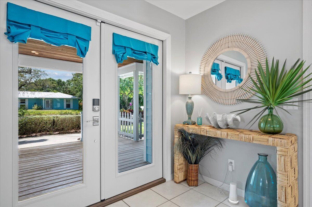 A modern entrance with a glass door, a wooden console table with decorative items, and a mirror on the wall. - Pool House 1/2 Mile From Downtown Stuart (Stuart)
