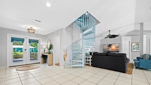 A spacious living room with a blue spiral staircase, a large grey sofa, and a television. - Pool House 1/2 Mile From Downtown Stuart (Stuart)