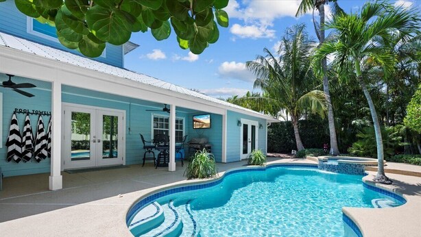 A poolside area with a blue pool, palm trees, and a building with a sign reading "POOL TOWELS". - Pool House 1/2 Mile From Downtown Stuart (Stuart)