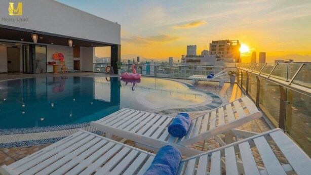 A rooftop pool with lounge chairs and a flamingo decoration, overlooking a cityscape at sunset. - Merry Land Hotel Da Nang (Da Nang Municipality)