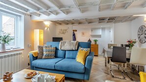 Uma sala de estar com sofá azul, mesa de centro de madeira e um espaço de refeições com cadeiras e mesa.