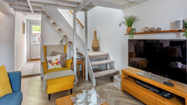 Uma sala de estar com escada, sofá, mesa de centro, televisão e uma planta.