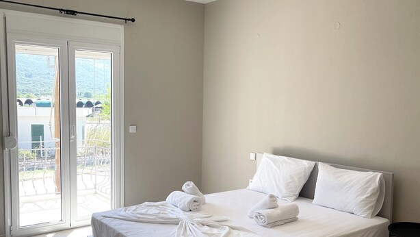 A modern hotel room with a large bed, white linens, and a view through the sliding glass doors. - Fairytale Apartments (Igoumenitsa)