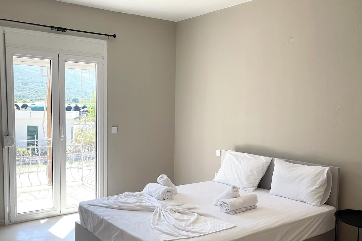 A modern hotel room with a large bed, white linens, and a view through the sliding glass doors.
