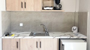 A compact kitchen with wooden cabinets, a built-in sink, and a white refrigerator. - Fairytale Apartments (Igoumenitsa)