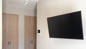A room with a flat-screen TV mounted on the wall, wooden wardrobes, and a light-colored floor. - Fairytale Apartments (Igoumenitsa)