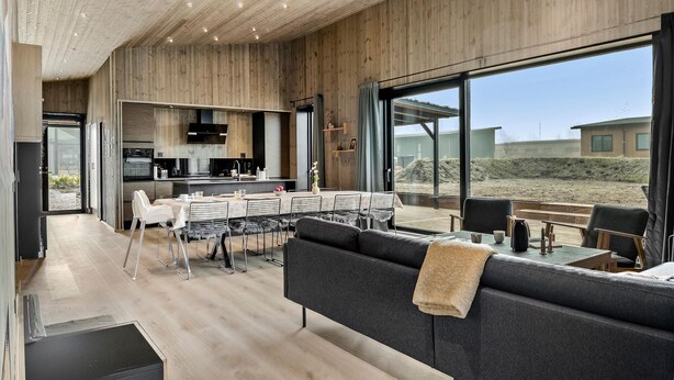 A modern kitchen with wooden walls and a dining area with a large window overlooking a sandy landscape.