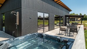 A modern house with a hot tub, outdoor seating, and a pergola.