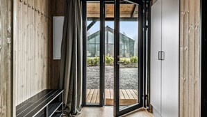 A modern interior with a wooden wall, a bench, a sliding glass door leading to an outdoor area with a gravel path and greenery.
