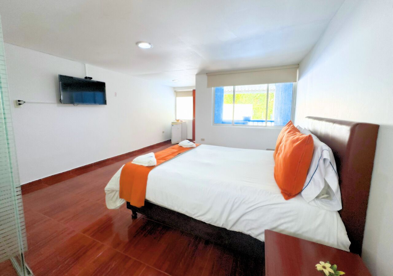 A hotel room with a bed, a window, a flat-screen TV, and a wooden floor.