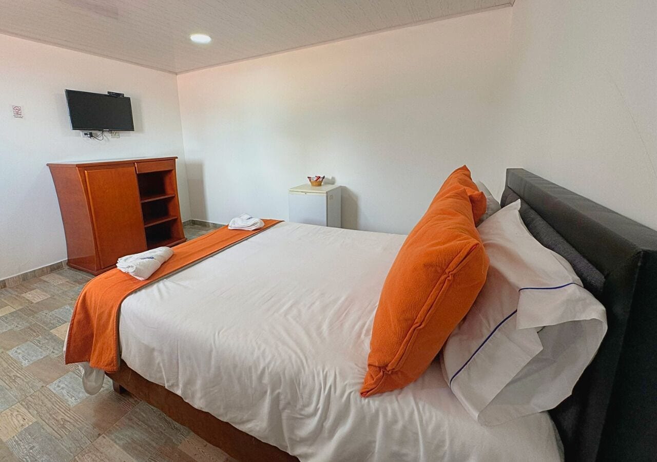 A hotel room with a bed, a TV, a wooden wardrobe, and a small table with a bowl.