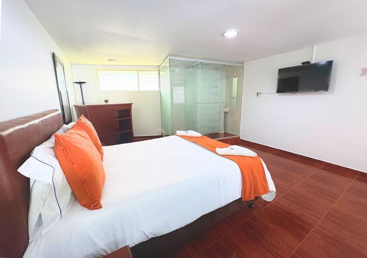 Una habitación de hotel con una cama grande, un televisor montado en la pared y suelo de madera.