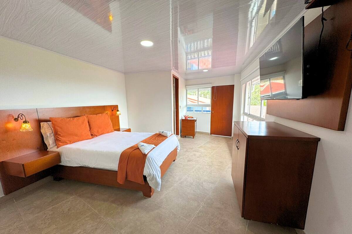 Un dormitorio con cama, mesita de noche y televisor montado en la pared.