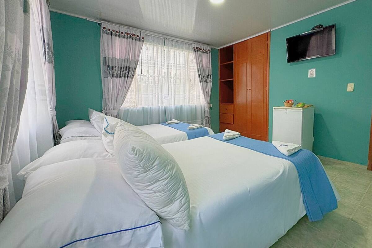 Una habitación de hotel con dos camas, un televisor en la pared y un mueble pequeño.
