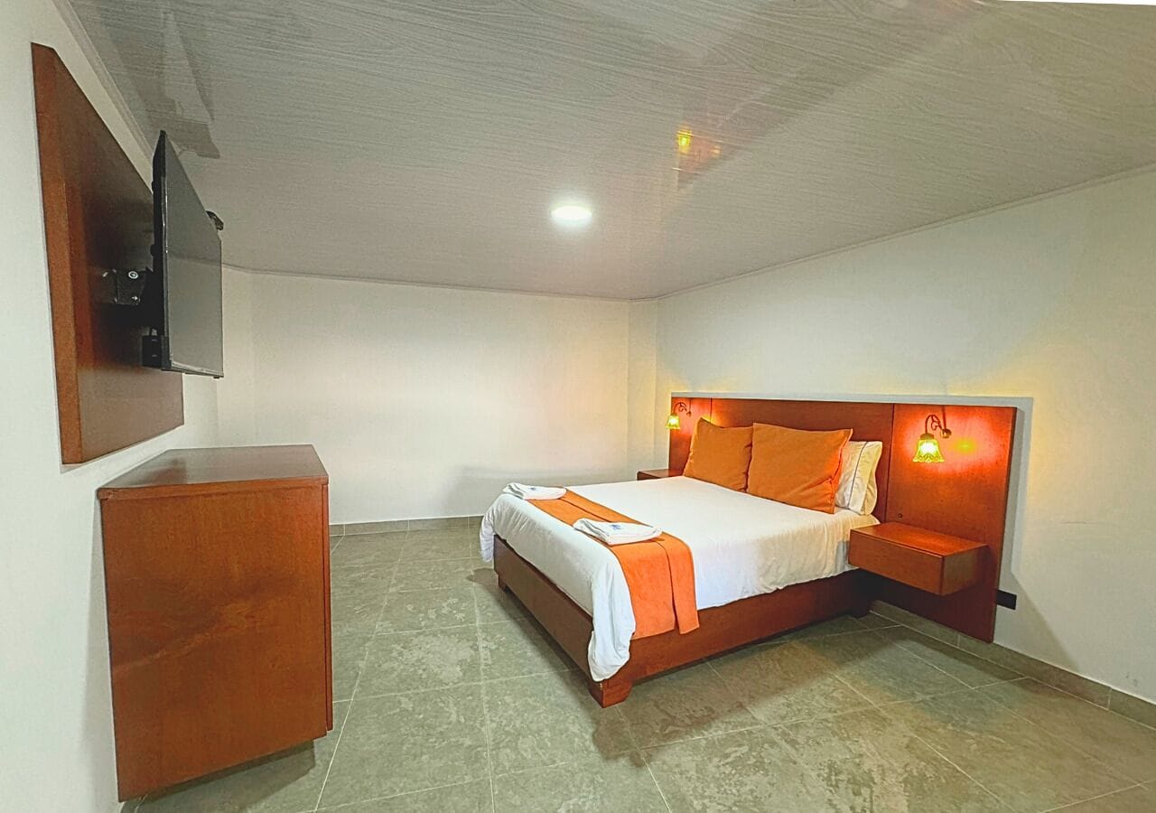 A bedroom with a bed, a wooden dresser, and a wall-mounted TV.