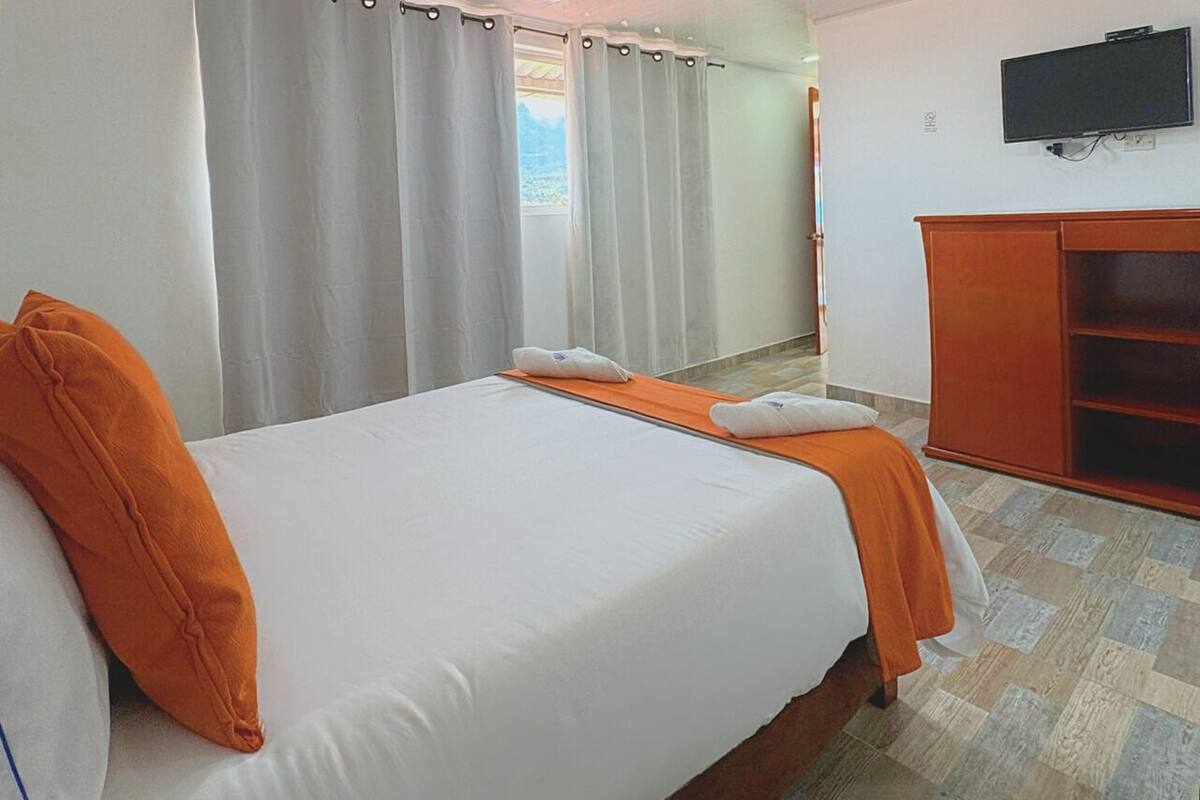 Una habitación de hotel con una cama grande, un armario de madera y un televisor en la pared.