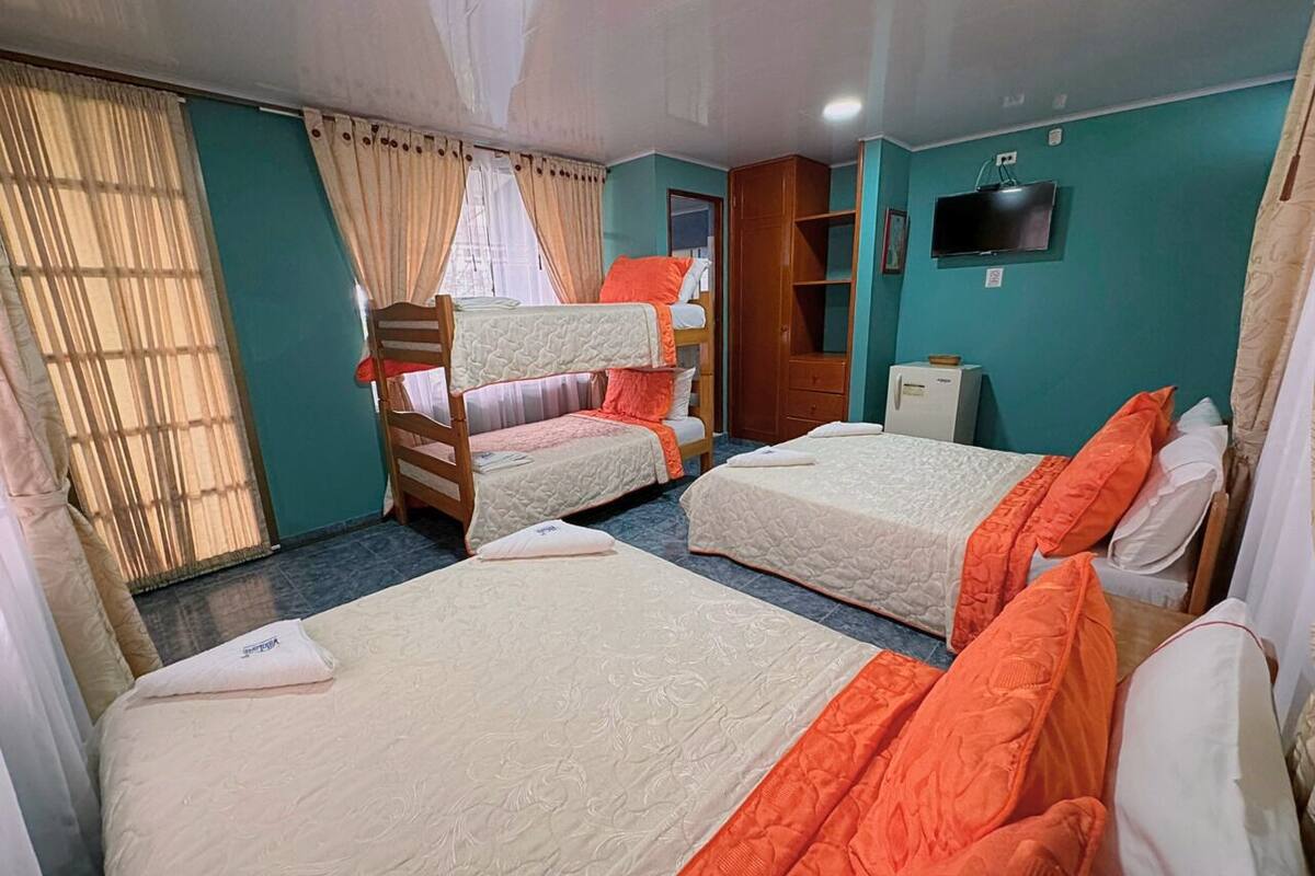 Habitación de hotel con tres camas, televisión, armario y escritorio.