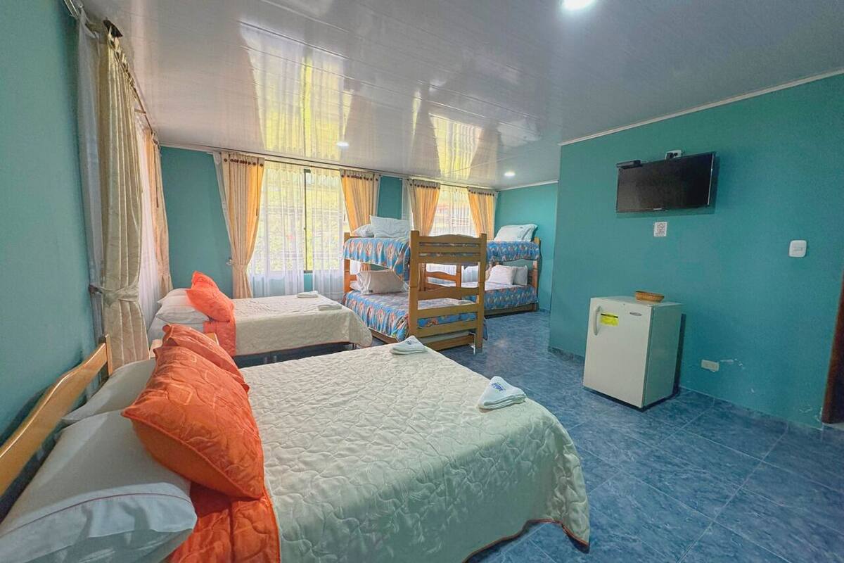 Una habitación con tres camas, un televisor en la pared y un refrigerador pequeño.