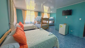 A room with three beds, a television on the wall, and a small refrigerator.