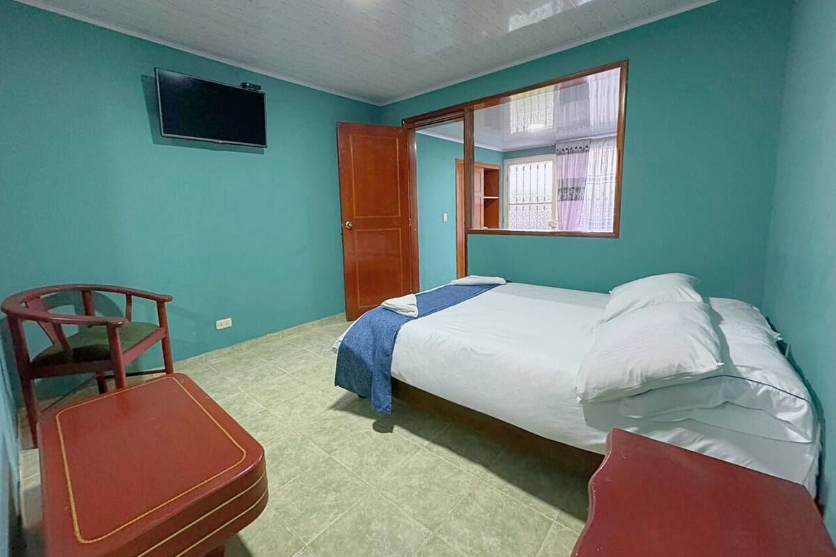 Una habitación con una cama, una silla, una mesita y un televisor en la pared.