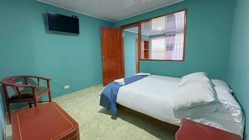 A room with a bed, a chair, a small table, and a television on the wall.