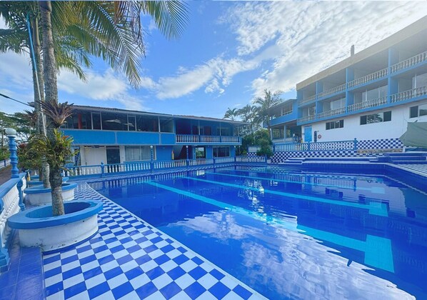 A swimming pool with a checkered floor, surrounded by a building with blue and white exterior walls and balconies. - VillaLoren Club Social y Deportivo (San Antonio del Tequendama)