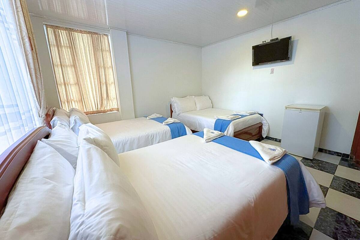 Habitación de hotel con tres camas, un televisor y un refrigerador pequeño.