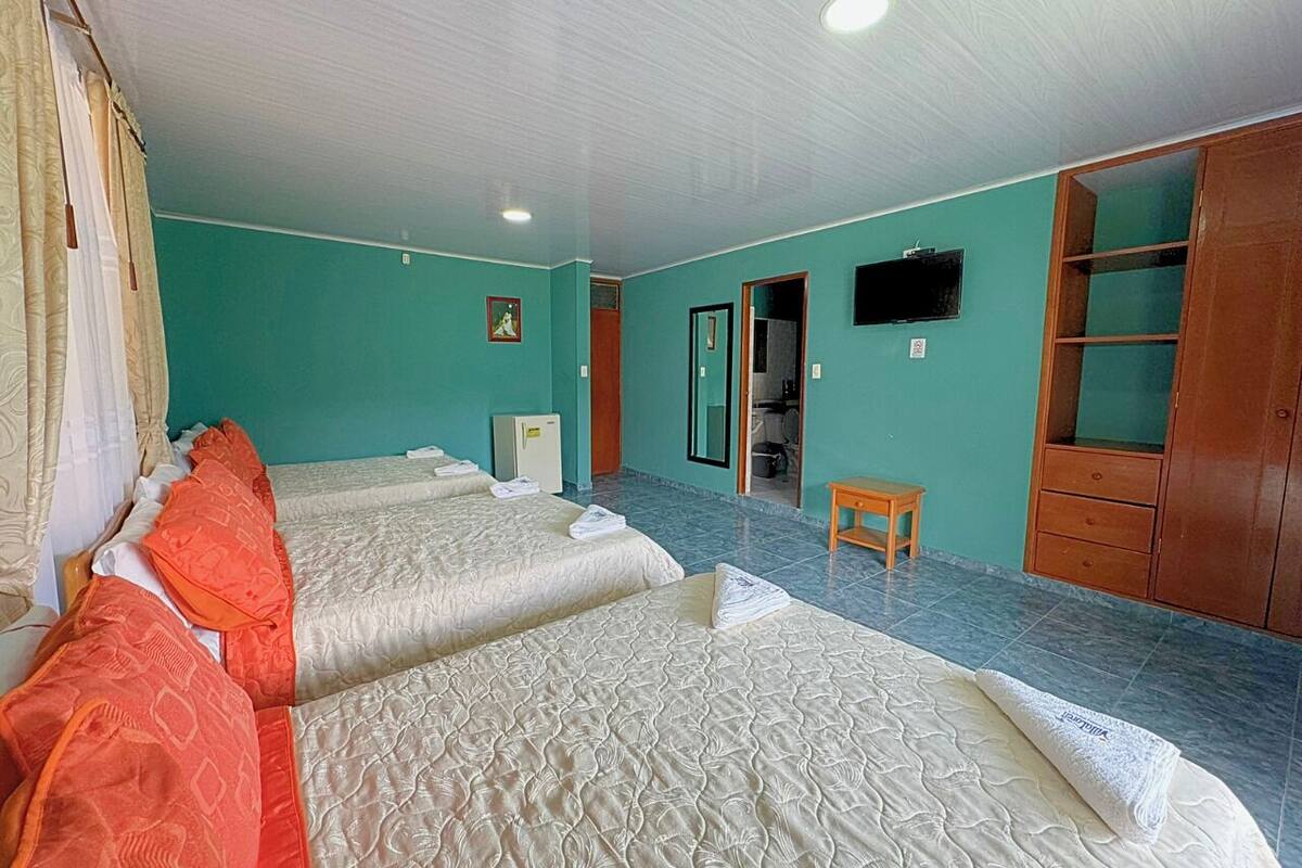 Habitación de hotel con dos camas, una mesita, un armario y un televisor en la pared.