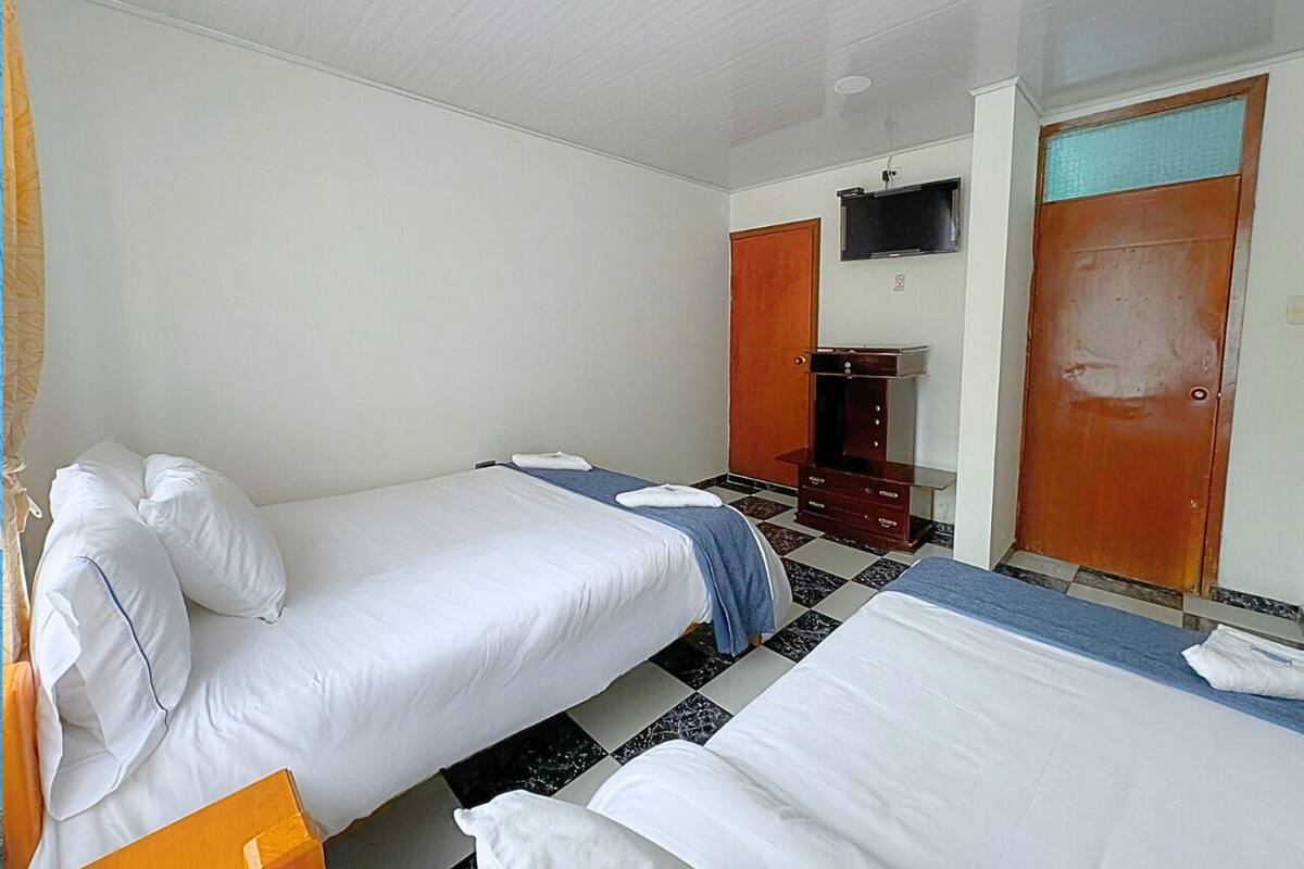 Habitación de hotel con dos camas individuales, un armario de madera, un televisor y suelo de baldosas.