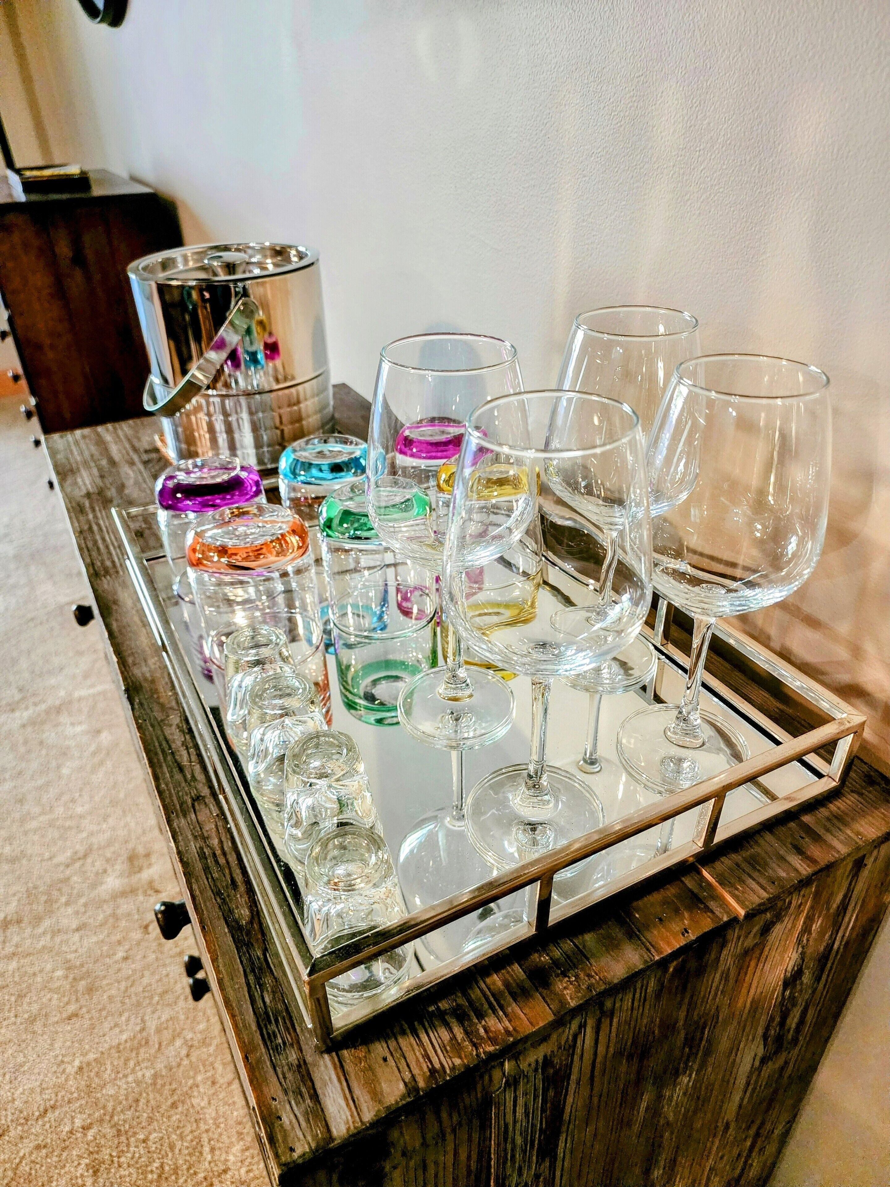 A tray with various wine glasses and tumblers on a reflective surface.