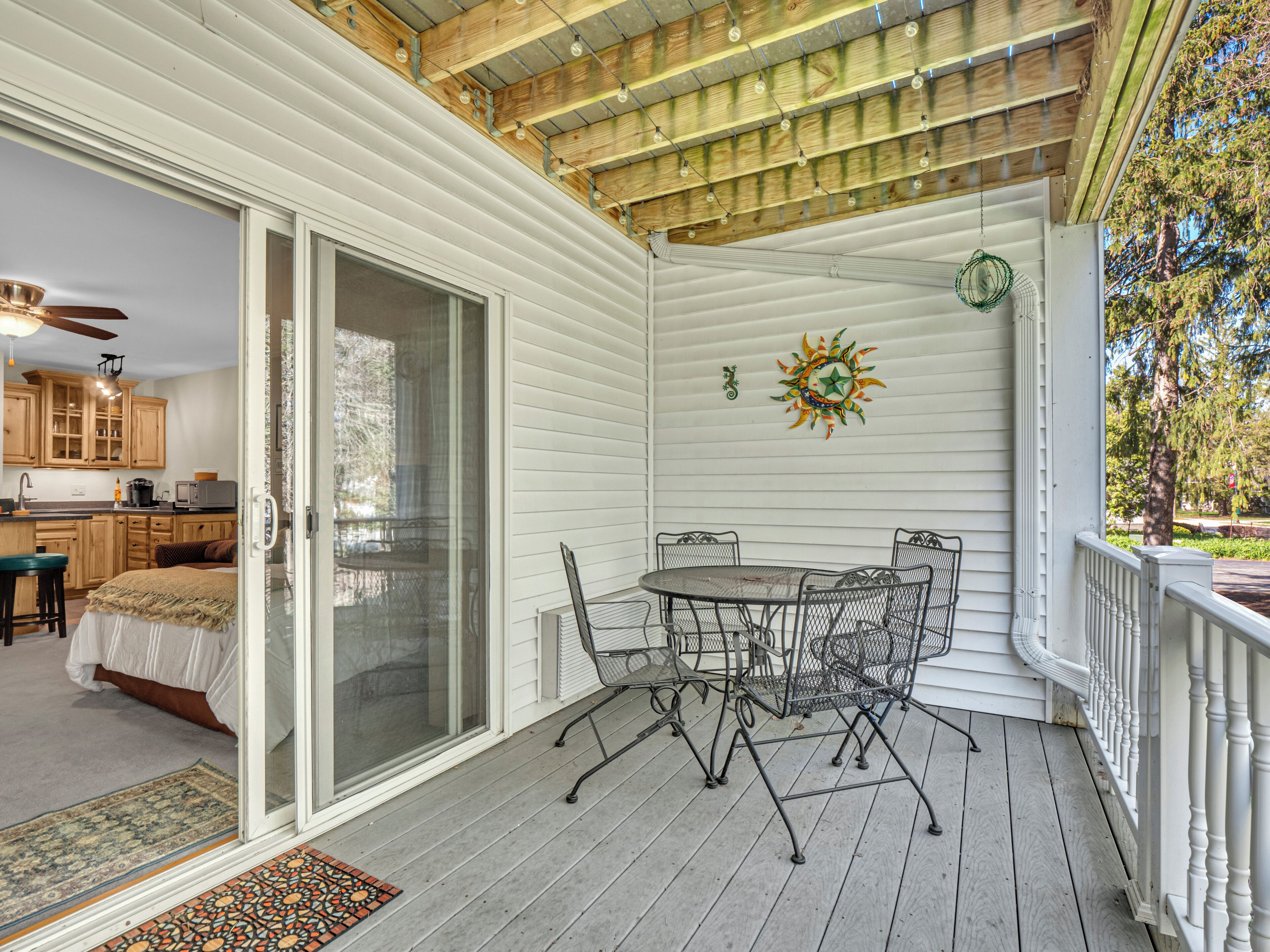 A covered porch with a dining table and chairs, a sliding glass door leading to a bedroom, and a kitchen visible through the door.